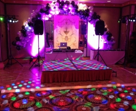 Indoor party stage setup with uplights, balloons, speakers, gobo projector and dance floor lighting.