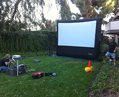 Crew sets up outdoor movie projector and inflatable screen.