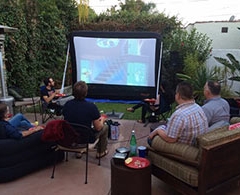 Group of guys watch outdoor movie on inflatable screen on patio.