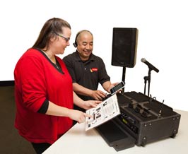 Tech support shows iPlay sound system to woman, including speakers, mixer and iPhone.