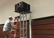 AV technician climbing ladder to install digital cinema projector