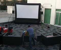 Man sets up outdoor movie viewing area with inflatable screen, sound system and projector.